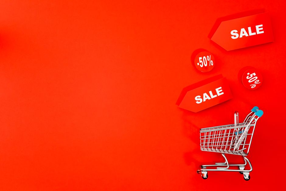 Carrinho de compras com etiquetas de desconto em um vibrante fundo vermelho promovendo promoções.